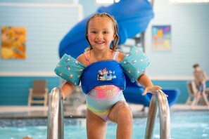 A child in a pool wearing a life jacket with cartoon characters. - Cozy Tall Timbers Retreat_Pvt Hot Tub_Near Lazy River_Free Tickets_Shuffleboard_Arcade (Hollister)
