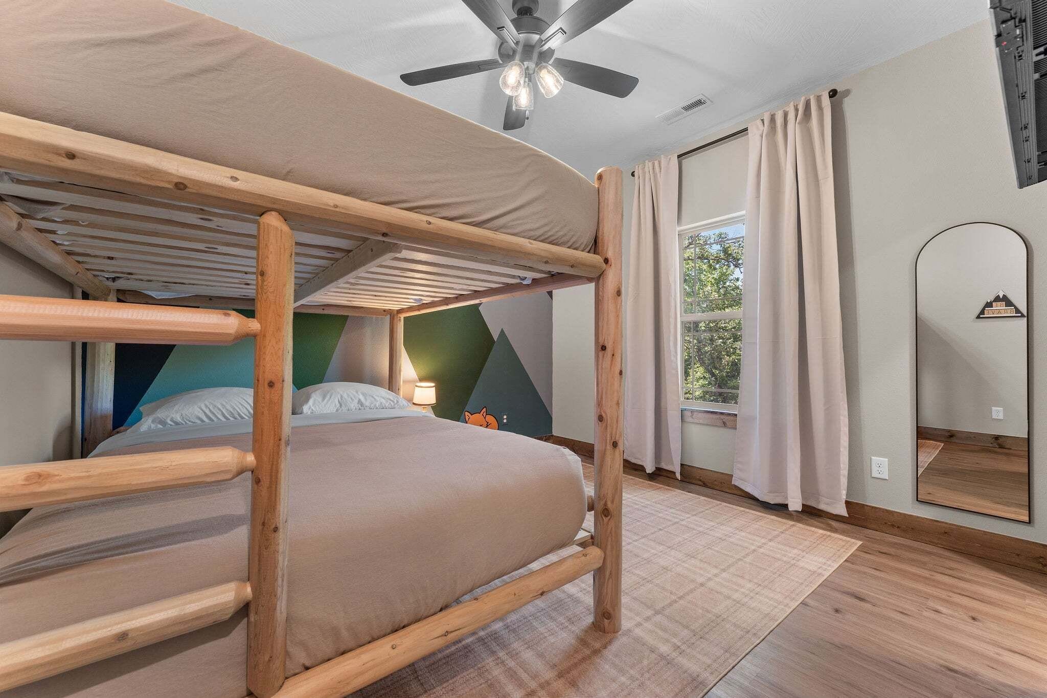 A bunk bed room with a ceiling fan, a window with curtains, and a mirror on the wall.
