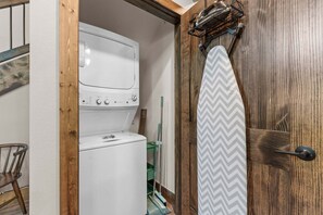 A laundry room with a stacked washer and dryer, a wooden door, and a green mop. - Cozy Tall Timbers Retreat_Pvt Hot Tub_Near Lazy River_Free Tickets_Shuffleboard_Arcade (Hollister)