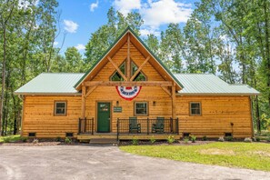 Une cabane en rondins avec une porte verte, une véranda avec deux chaises et un drapeau au-dessus de l’entrée.