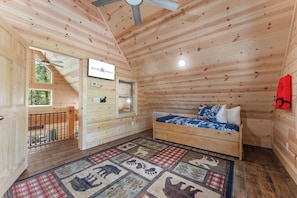A cozy wooden cabin interior with a bed, a small desk, and a window overlooking a forest. - Cabin Near Thunder Ridge & Big Cedar_Private Hot Tub_Free Attraction Tickets_Bonus Loft (Ridgedale)