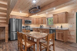 A modern kitchen with wooden cabinets, stainless steel appliances, and a glass-top dining table. - Cabin Near Thunder Ridge & Big Cedar_Private Hot Tub_Free Attraction Tickets_Bonus Loft (Ridgedale)