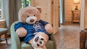 A plush teddy bear seated on a green armchair in a room with wooden walls and a wooden floor. - Cabin Near Thunder Ridge & Big Cedar_Private Hot Tub_Free Attraction Tickets_Bonus Loft (Ridgedale)