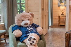 Ein kuscheliger Teddybär sitzt auf einem grünen Sessel in einem Raum mit Holzwänden und Holzboden.