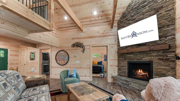 A cozy cabin interior with a stone fireplace, wooden walls, and a dining area. - Cabin Near Thunder Ridge & Big Cedar_Private Hot Tub_Free Attraction Tickets_Bonus Loft (Ridgedale)