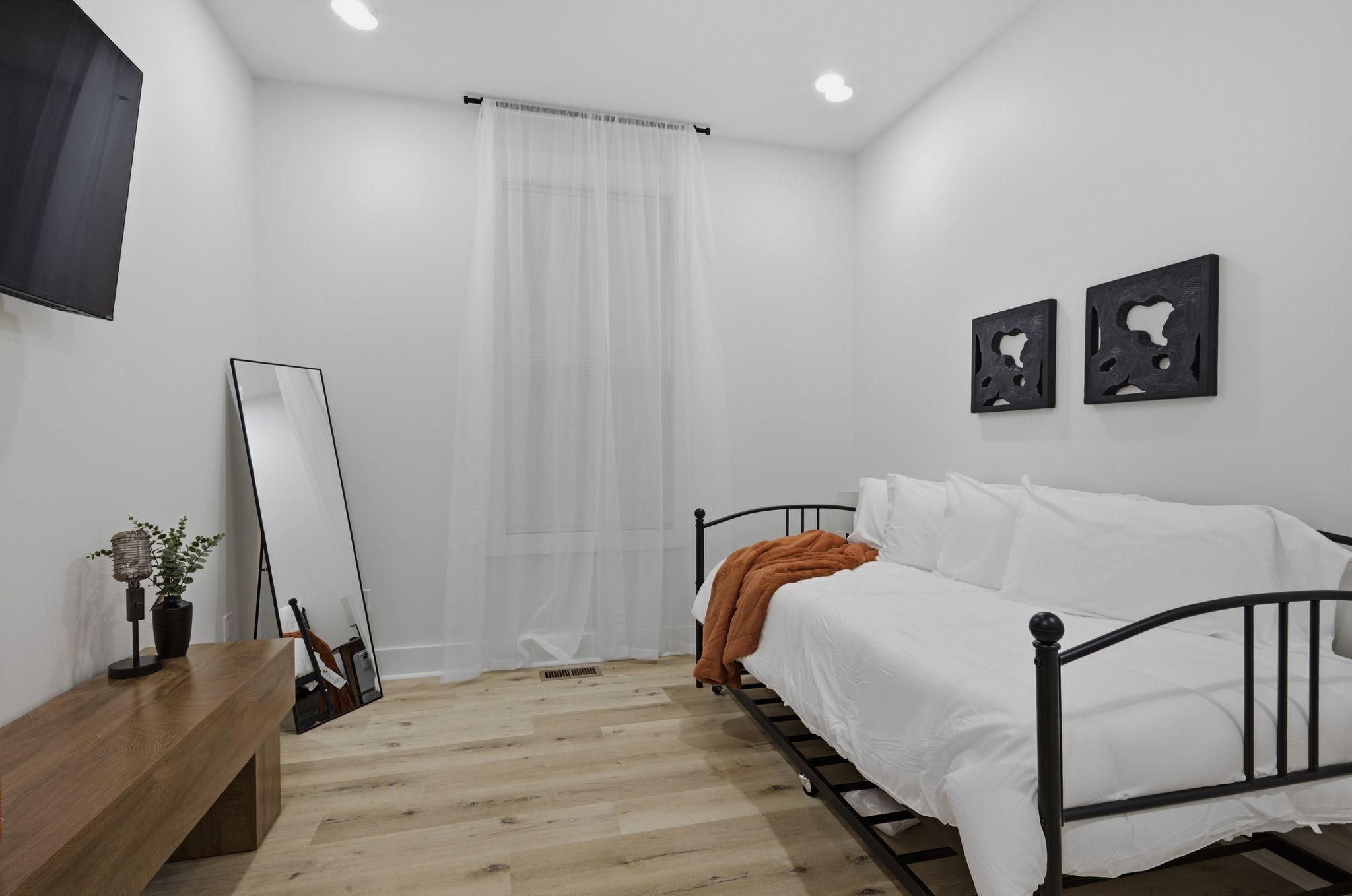 A bedroom with a bed, a bedside table, a mirror, and a wall-mounted artwork.