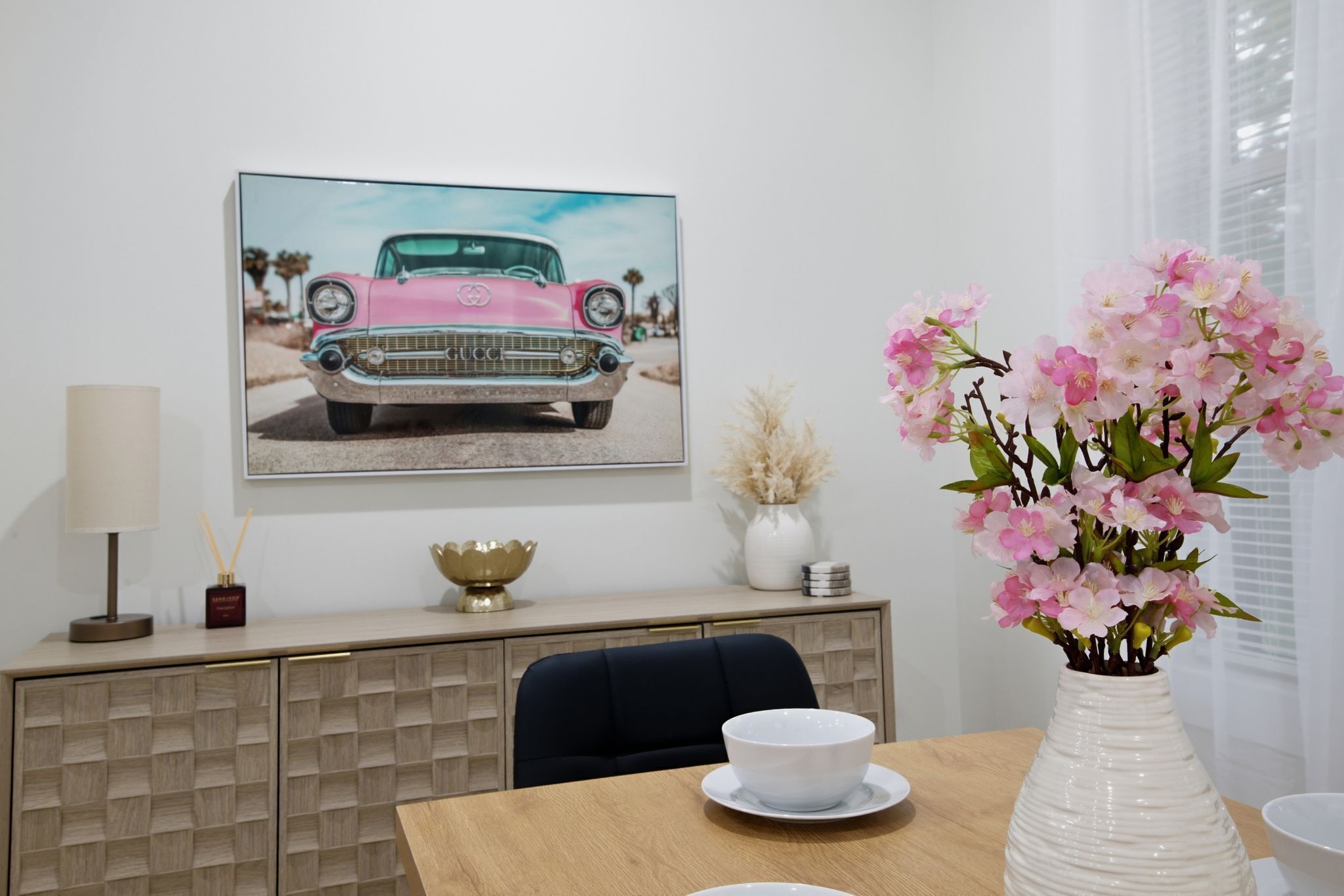 A dining area with a table, chairs, a vase of flowers, a cabinet, and a framed picture on the wall.