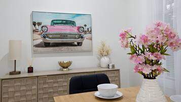 A dining area with a table, chairs, a vase of flowers, a cabinet, and a framed picture on the wall.
