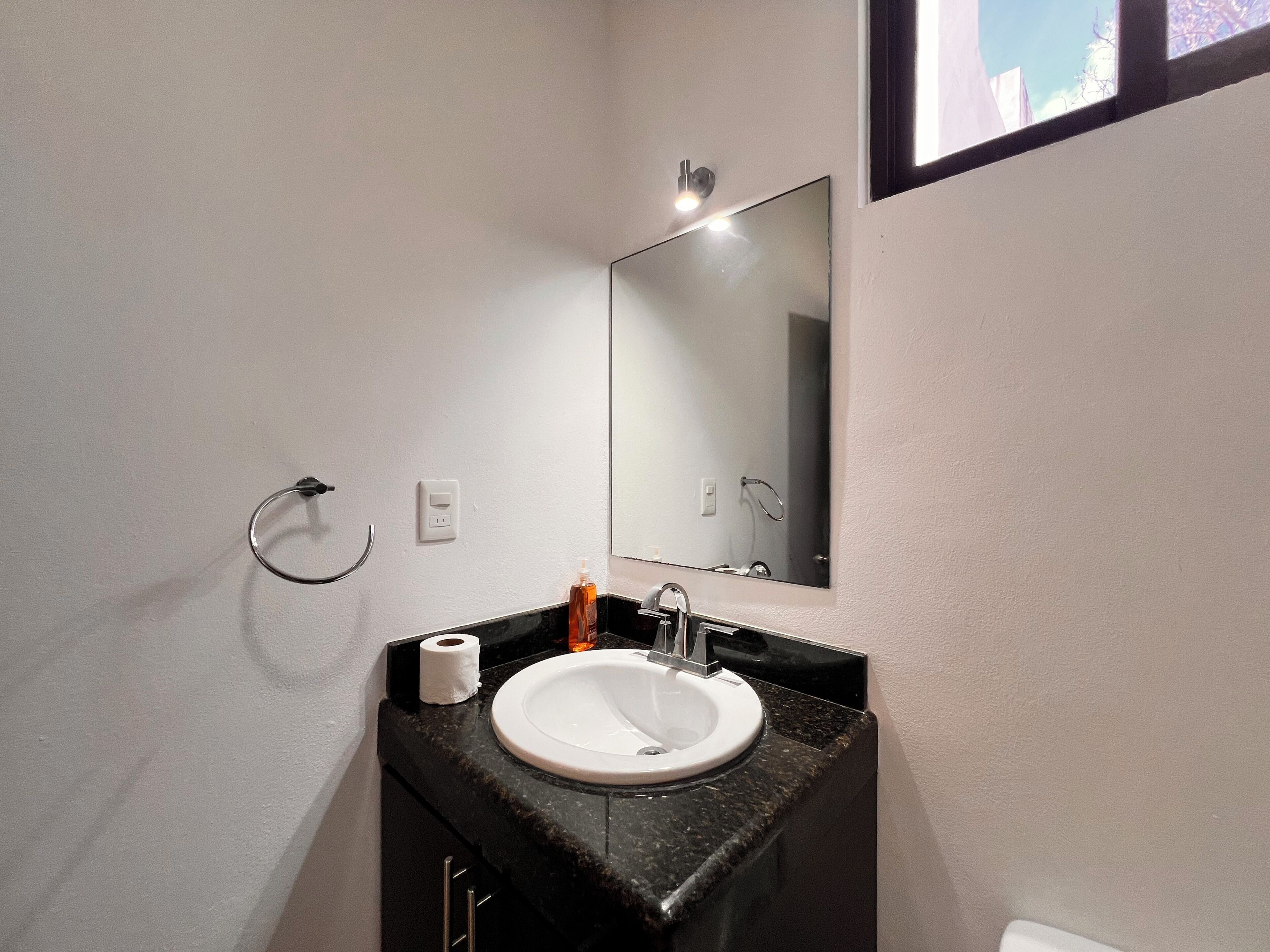 Ein Badezimmer mit einem weißen Waschbecken, einem Spiegel, einem Handtuchhalter und einem Toilettenpapierrollenhalter.
