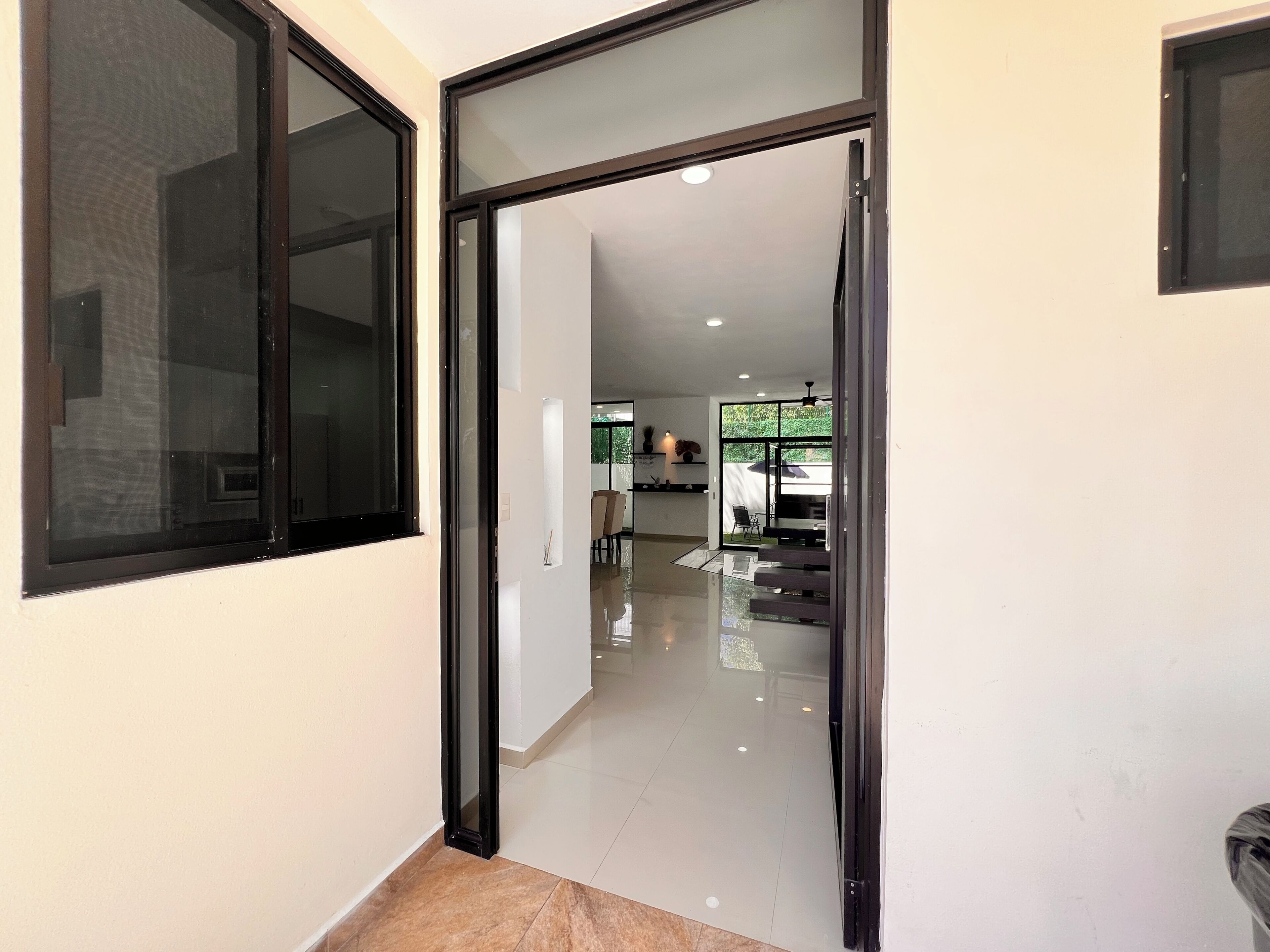 A hallway leading to a dining area with a glass partition, a ceiling fan, and a tiled floor.