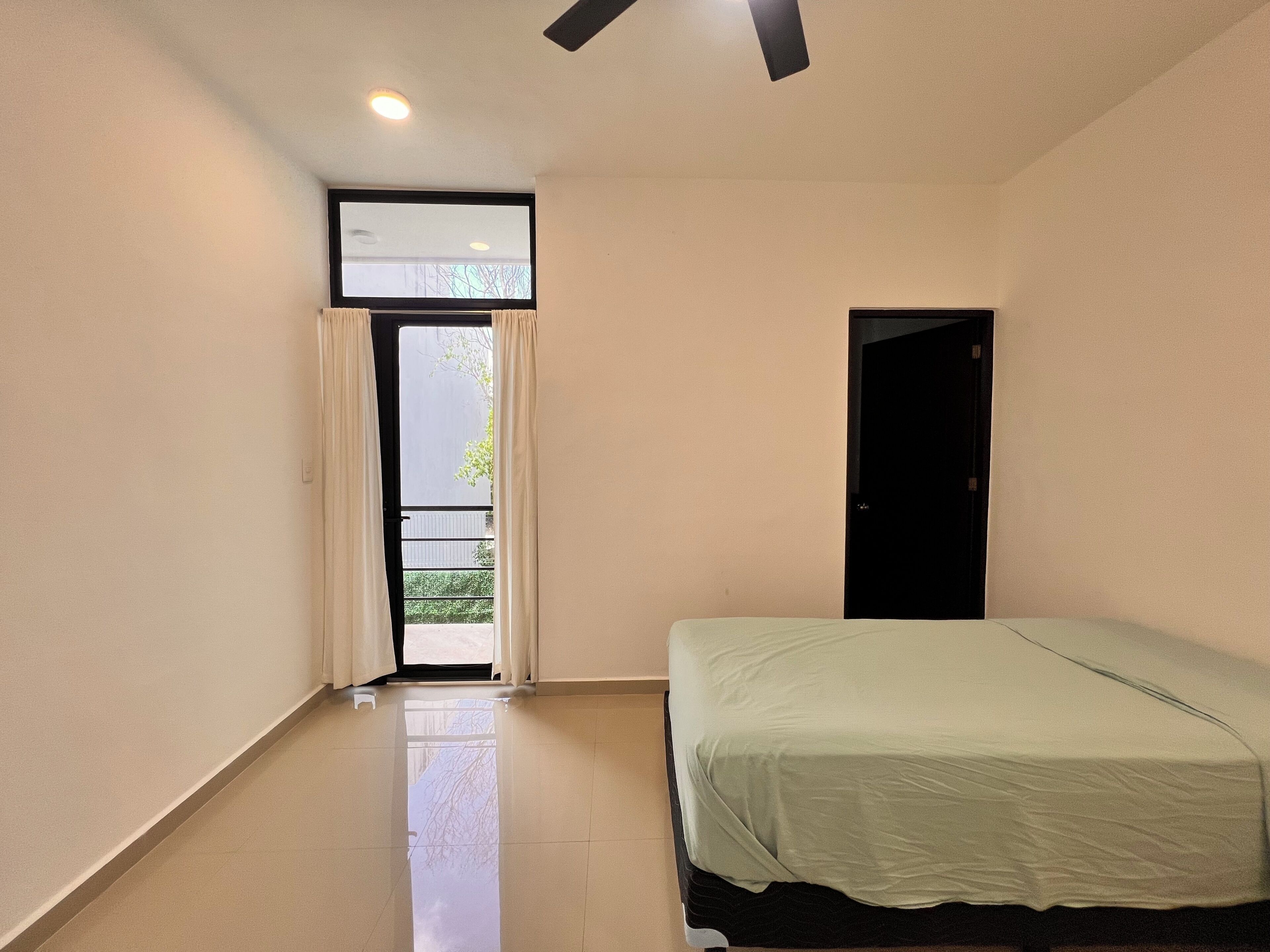 A bedroom with a bed, a door, a window with curtains, and a ceiling fan.