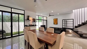 A modern interior with a dining area, a sofa, a staircase, and a view of the outdoors.