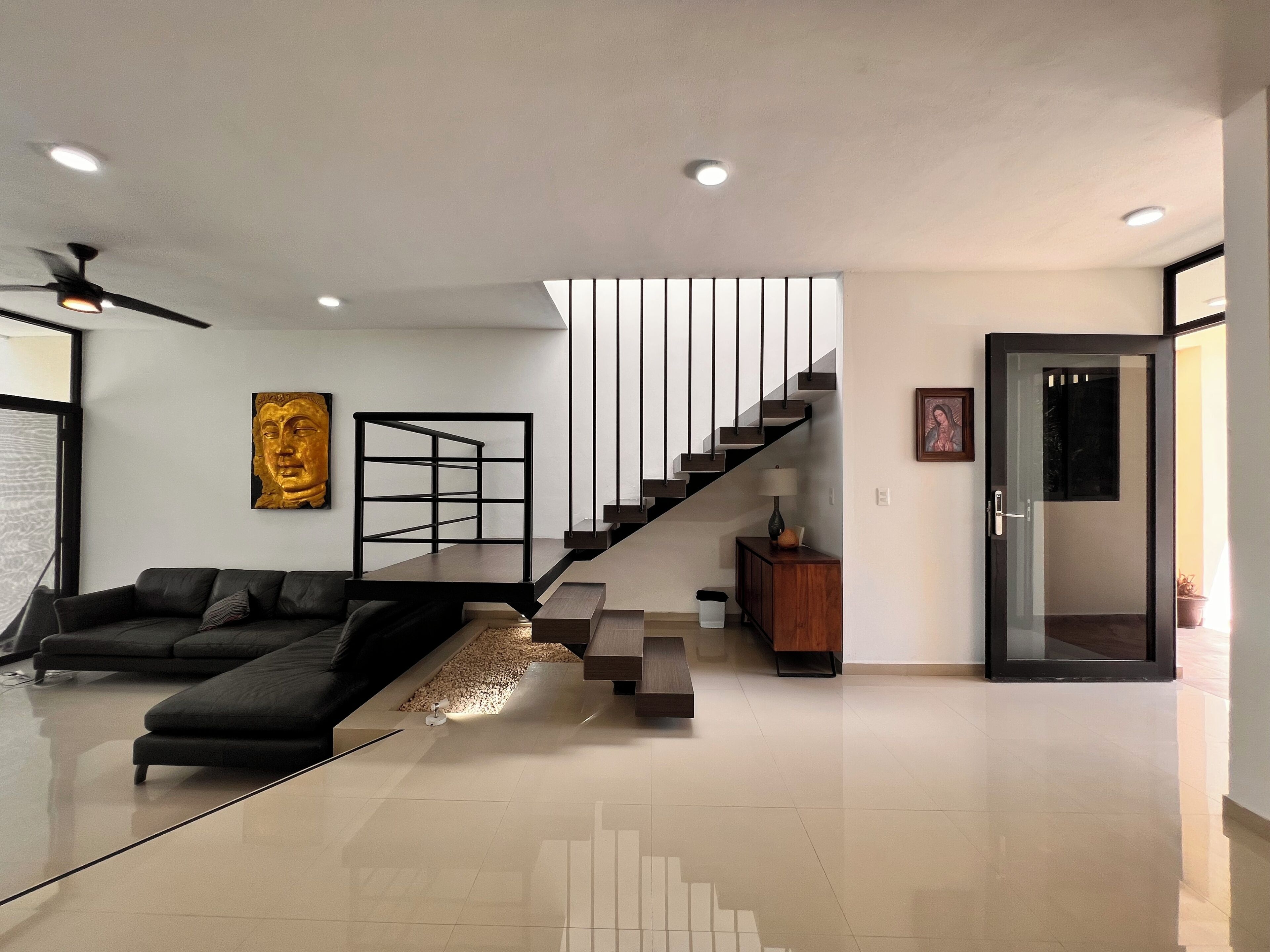 A modern living room with a black sofa, a glass coffee table, a staircase, and a minimalist design.