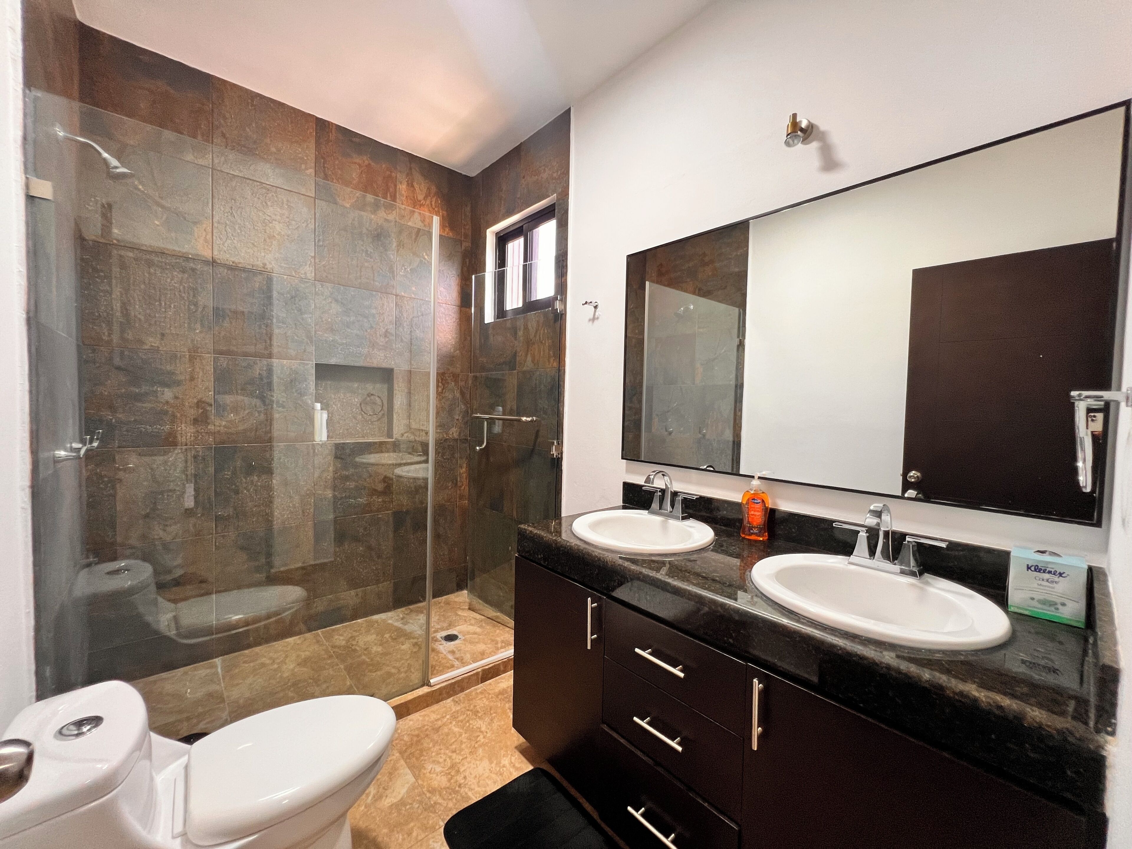 A bathroom with a glass shower enclosure, two sinks, a toilet, and a large mirror.