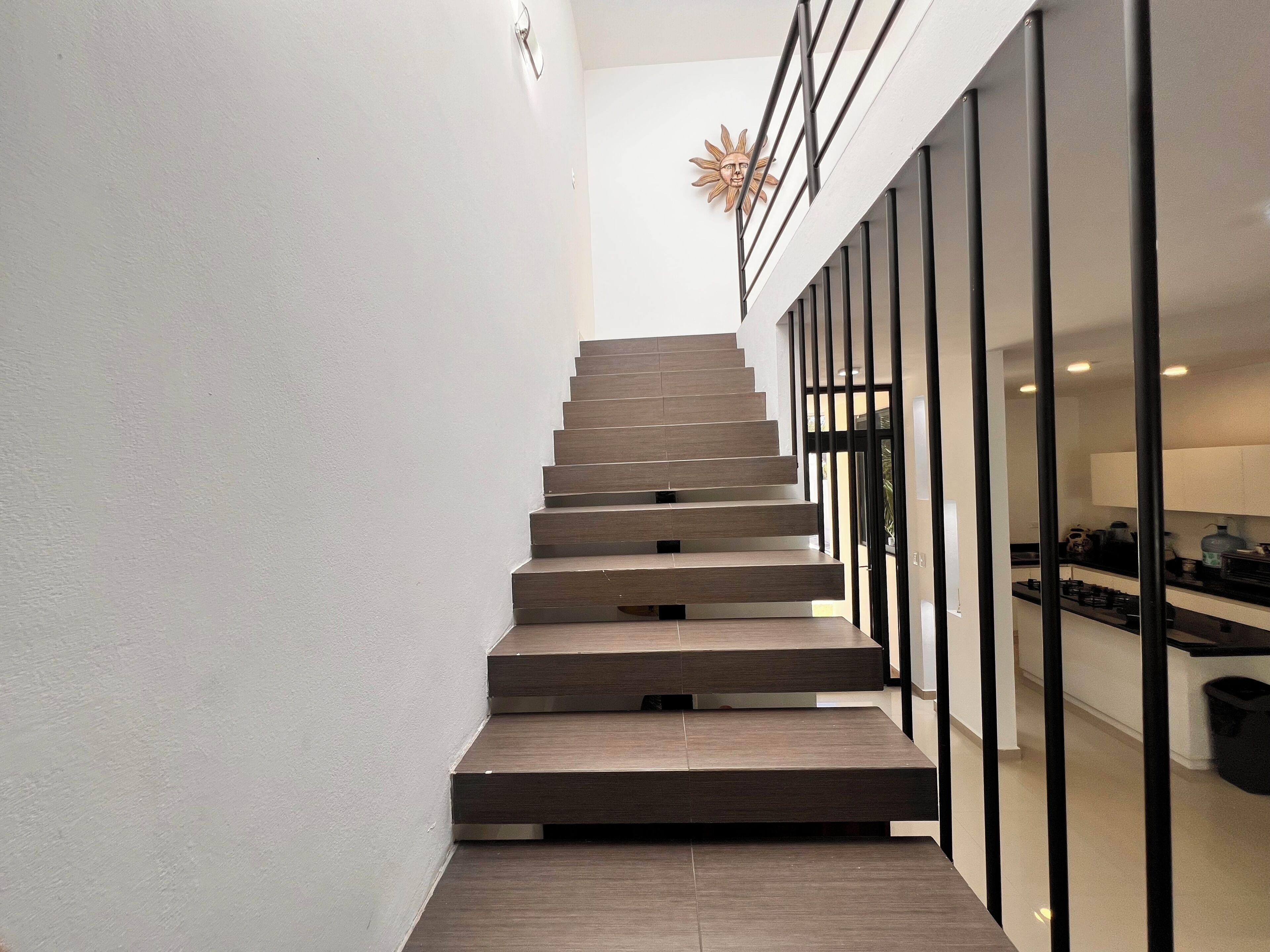 A modern staircase with a minimalist design, leading to a kitchen area with a black countertop and white cabinets.