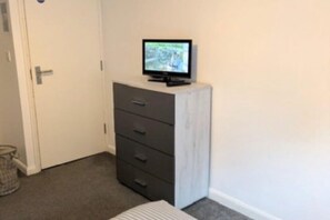A room with a white door, a grey cabinet with drawers, and a television on top.