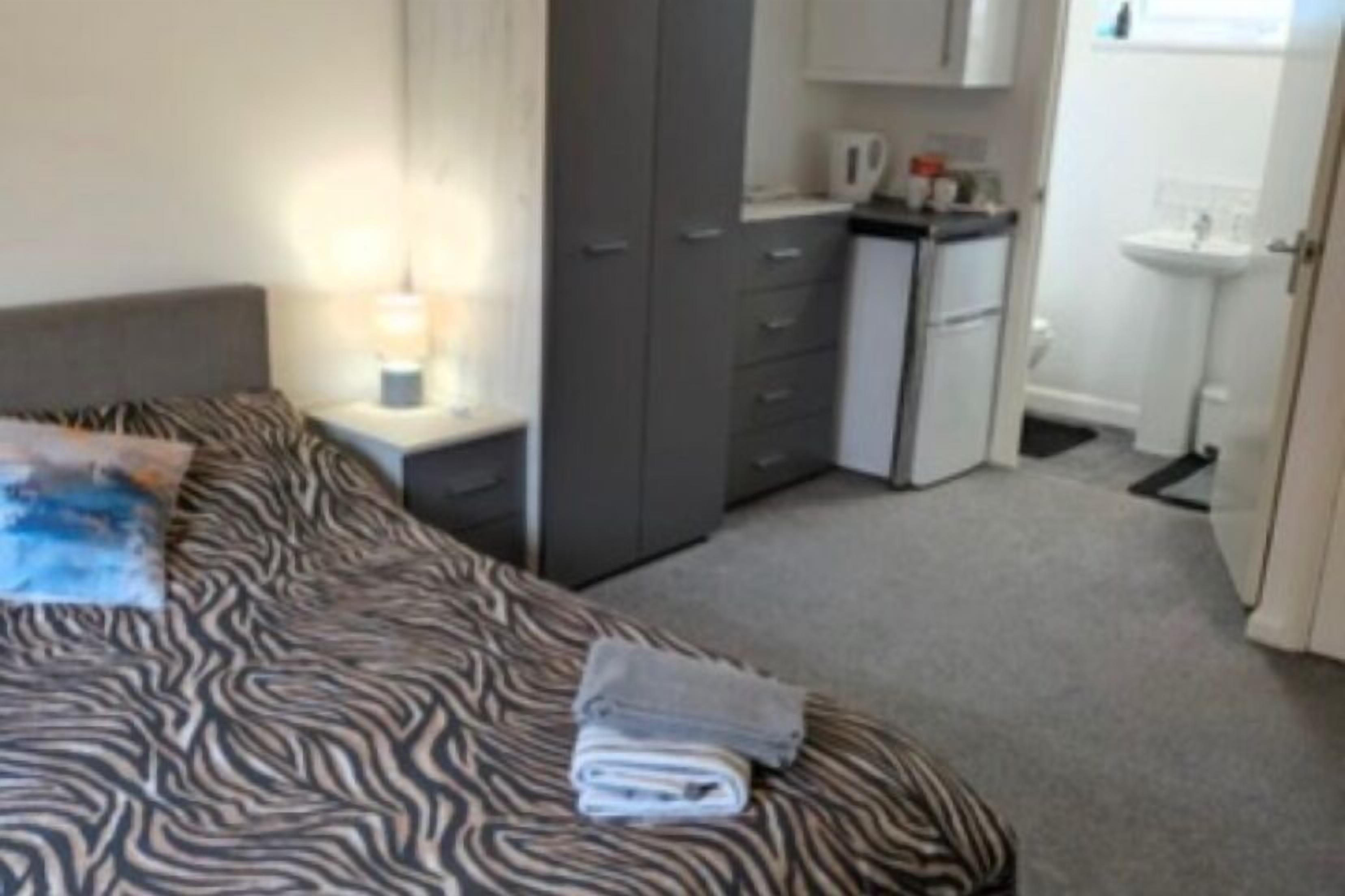 Une chambre comprenant un lit, une table de chevet, une armoire, un petit coin cuisine et une salle de bain.