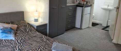 Une chambre comprenant un lit, une table de chevet, une armoire, un petit coin cuisine et une salle de bain.