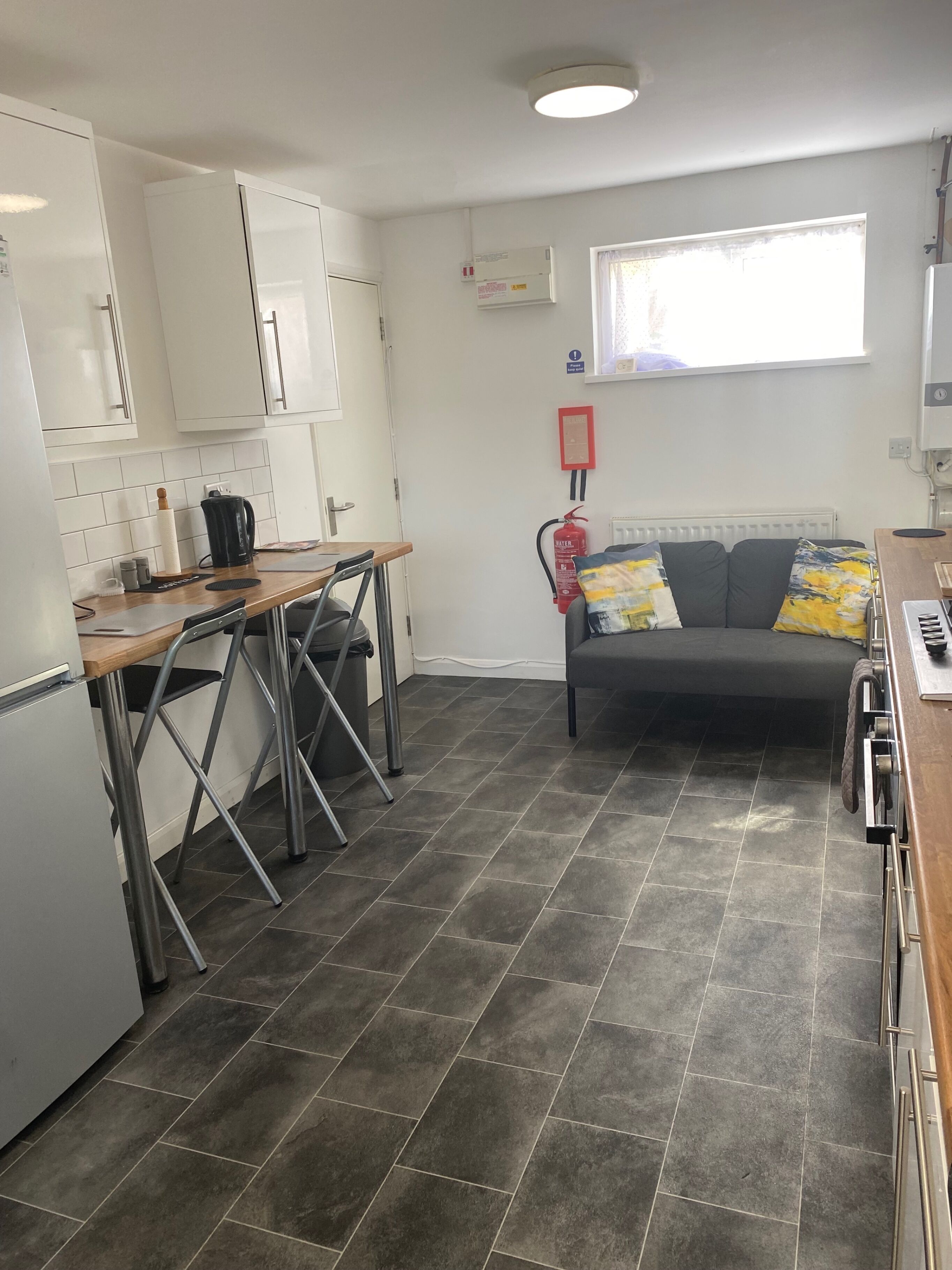 A compact kitchen with a dining area, a grey tiled floor, and a window with a view.
