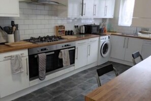 A kitchen with a stove, oven, washing machine, and a wooden countertop.