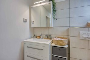 A modern bathroom with a white vanity, a mirror, a sink, and a small cabinet. - Studio with terrace and air conditioning (Poreč)