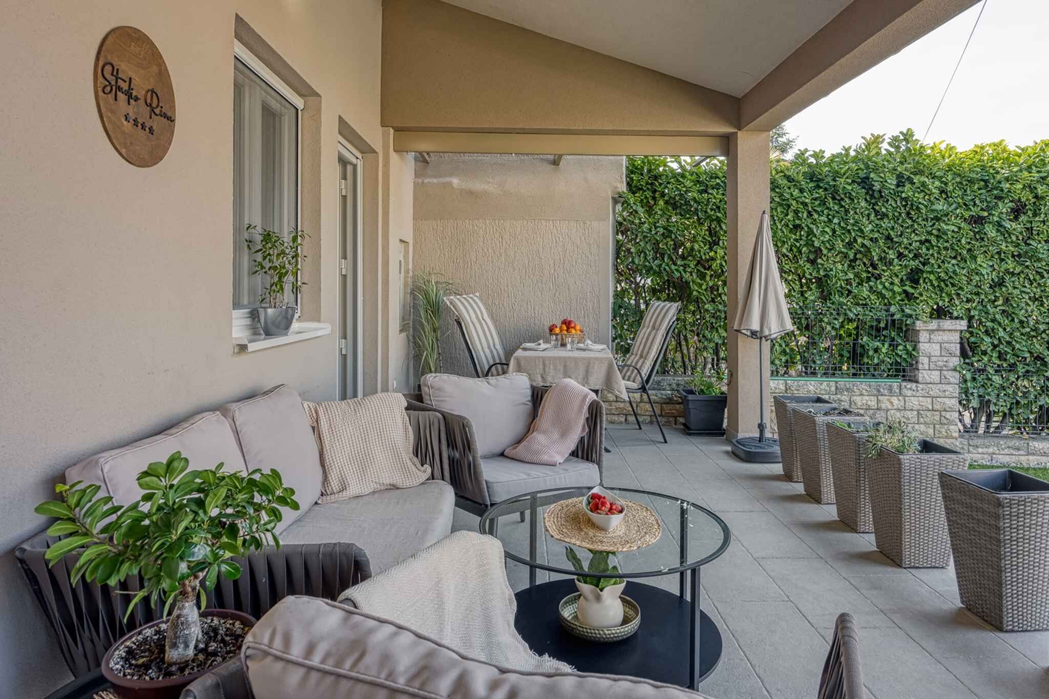 A covered outdoor seating area with a sofa, chairs, a table, and potted plants.