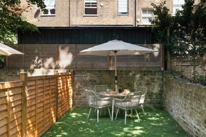 A patio with a table and chairs, a wooden fence, and a brick wall.