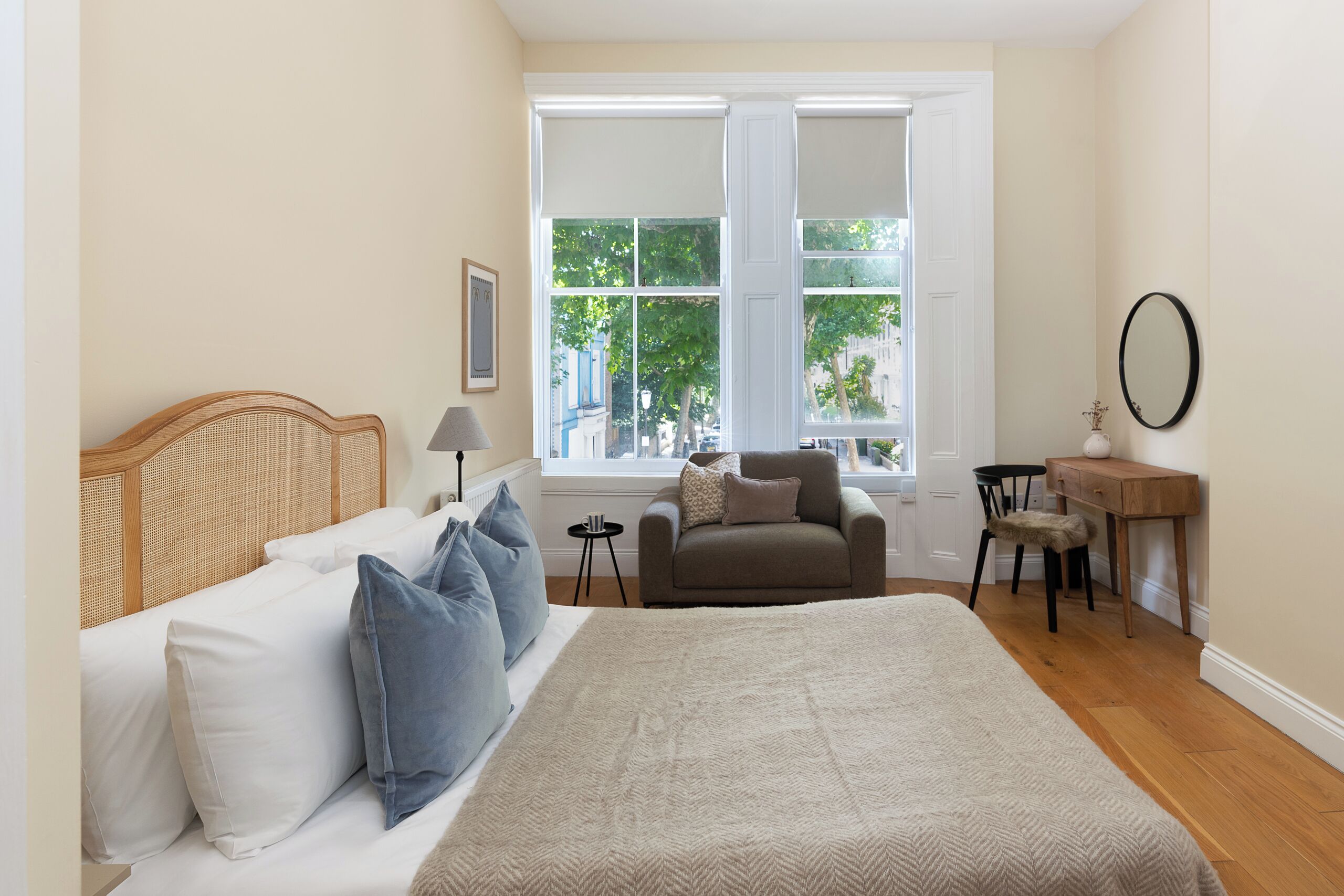 Een slaapkamer met een bed, een stoel, een bureau en een raam met uitzicht op groen.