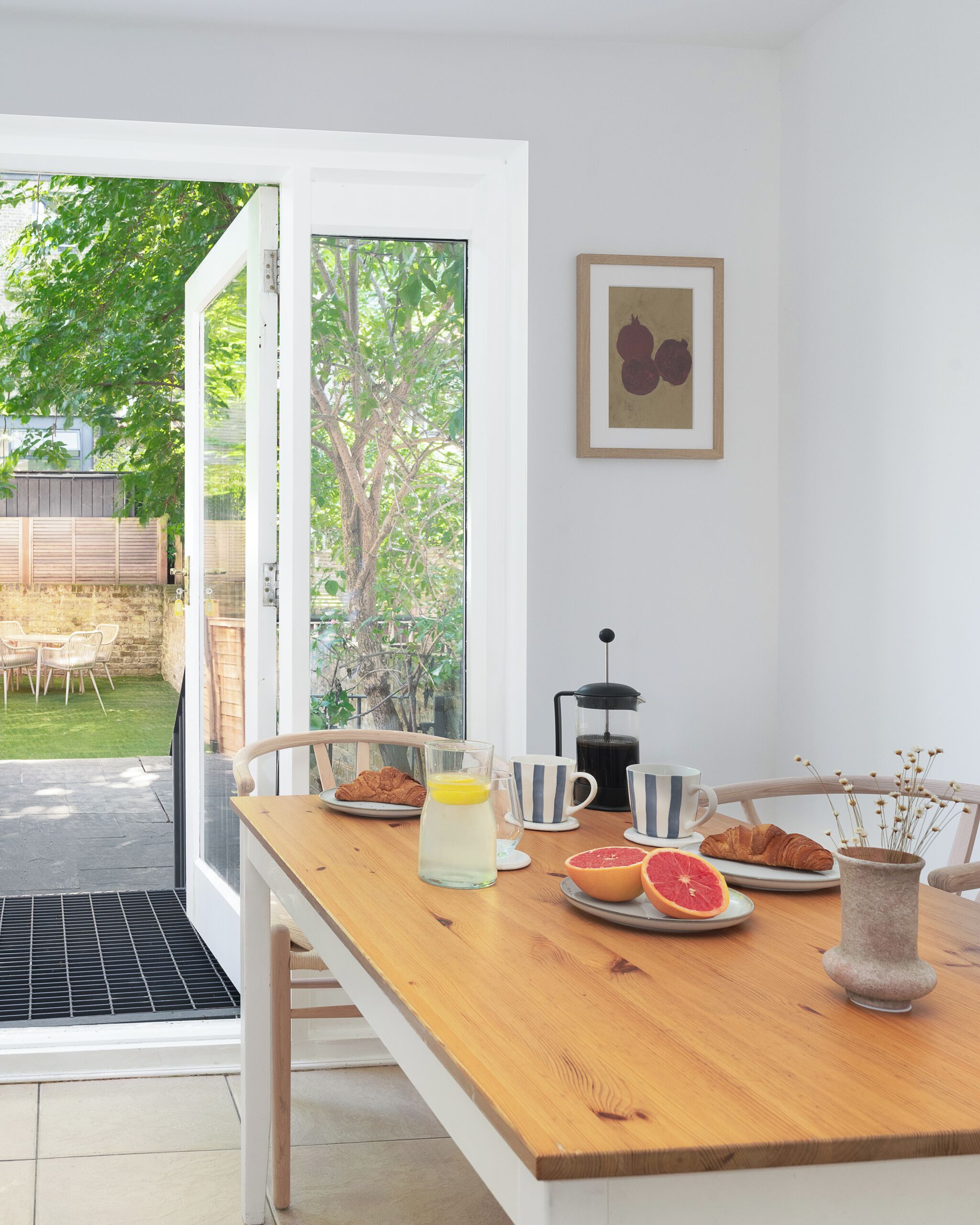 Un comedor con mesa de madera, sillas, cafetera y planta en maceta.