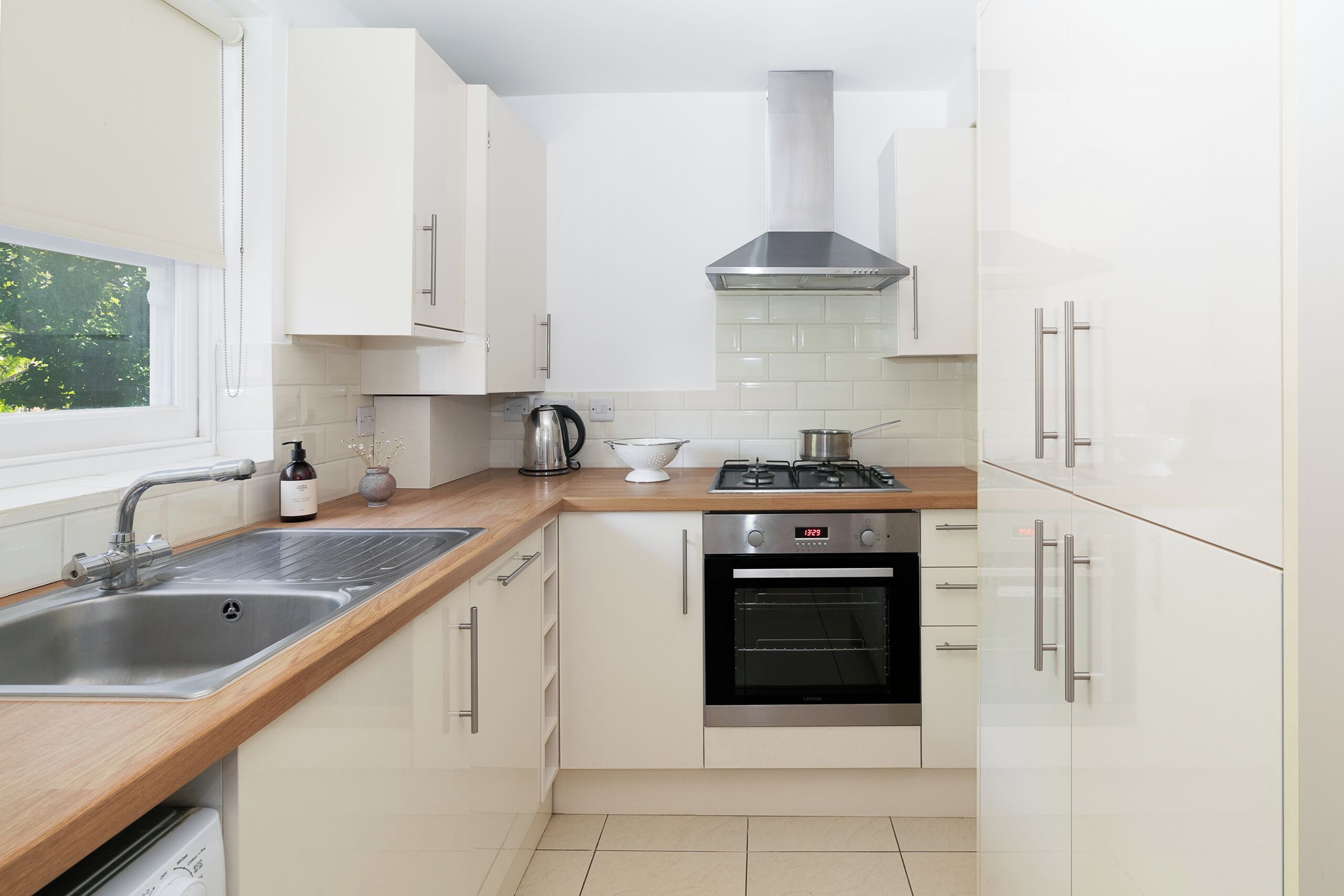 Une cuisine moderne avec des meubles blancs, un évier en acier inoxydable, une cuisinière à gaz et un four.
