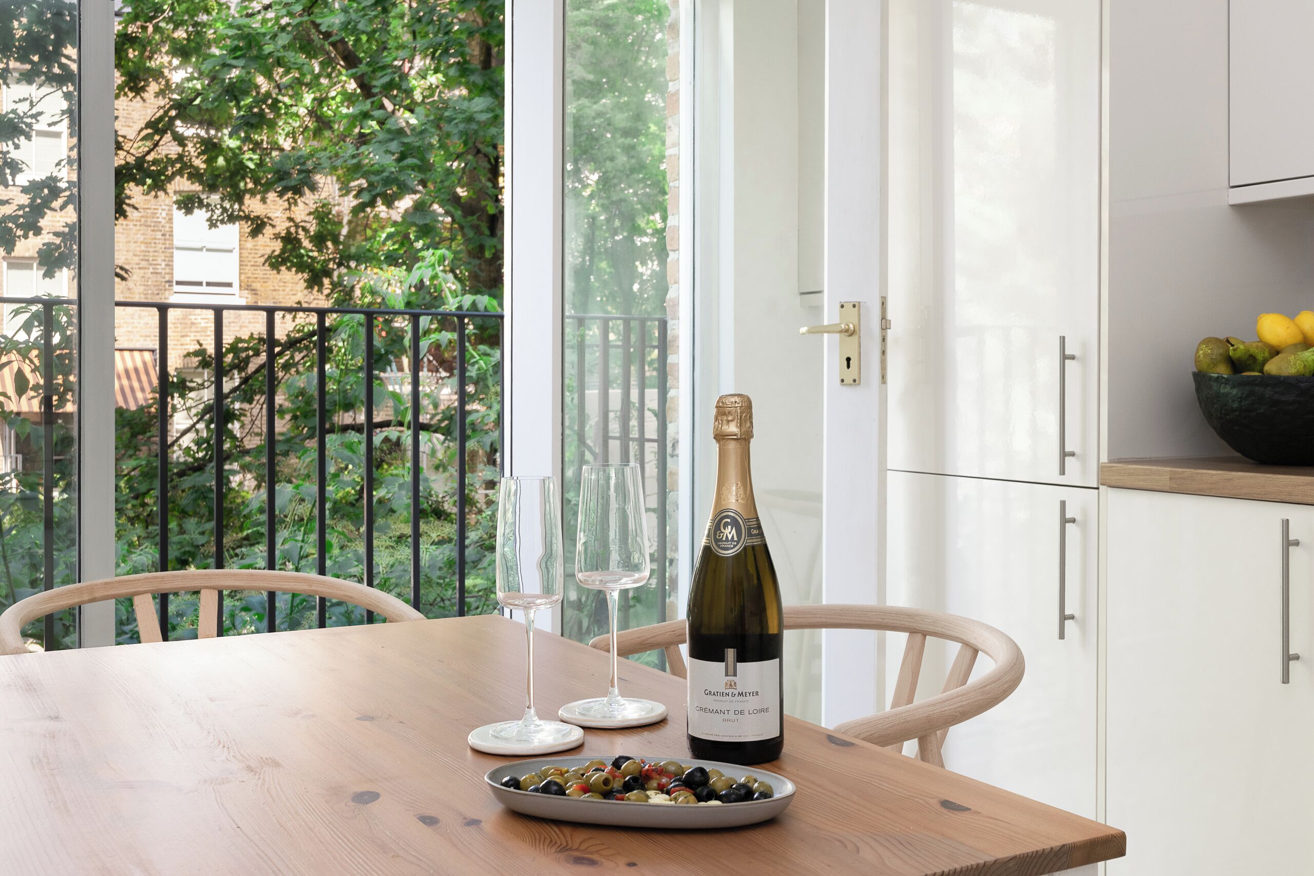 Une table en bois avec une bouteille de vin, deux verres à vin et un bol d’olives.