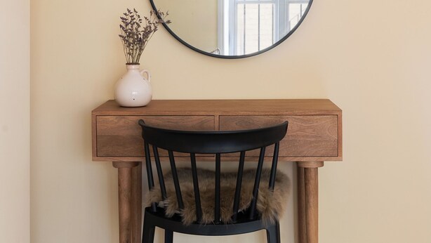 A wooden desk with a black chair, a white vase with dried flowers, and a round mirror on the wall. - Notting Hill Grove Apartments (London)