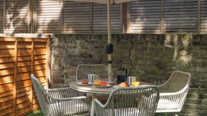 An outdoor patio with a round table, four wicker chairs, and a large umbrella. - Notting Hill Grove Apartments (London)