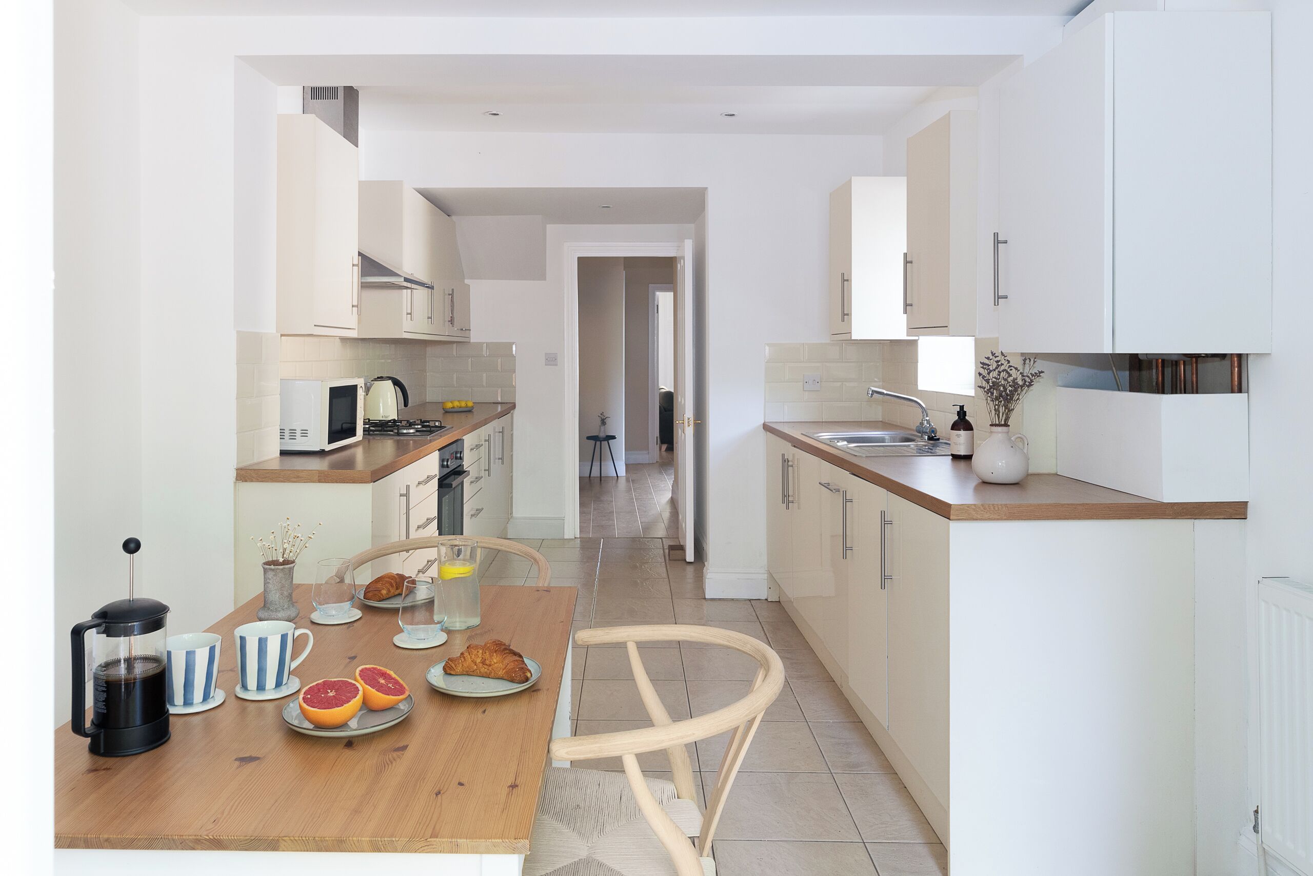 A modern kitchen with white cabinetry, a wooden dining table, and a chair.