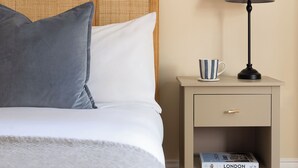 A neatly made bed with a grey blanket and pillows, a bedside table with a lamp and a striped mug, and a book titled 'LONDON' on the shelf. - Notting Hill Grove Apartments (London)