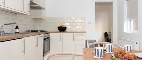 Une cuisine moderne avec des meubles blancs, un plan de travail en bois et un coin repas où une table est dressée pour le petit-déjeuner.