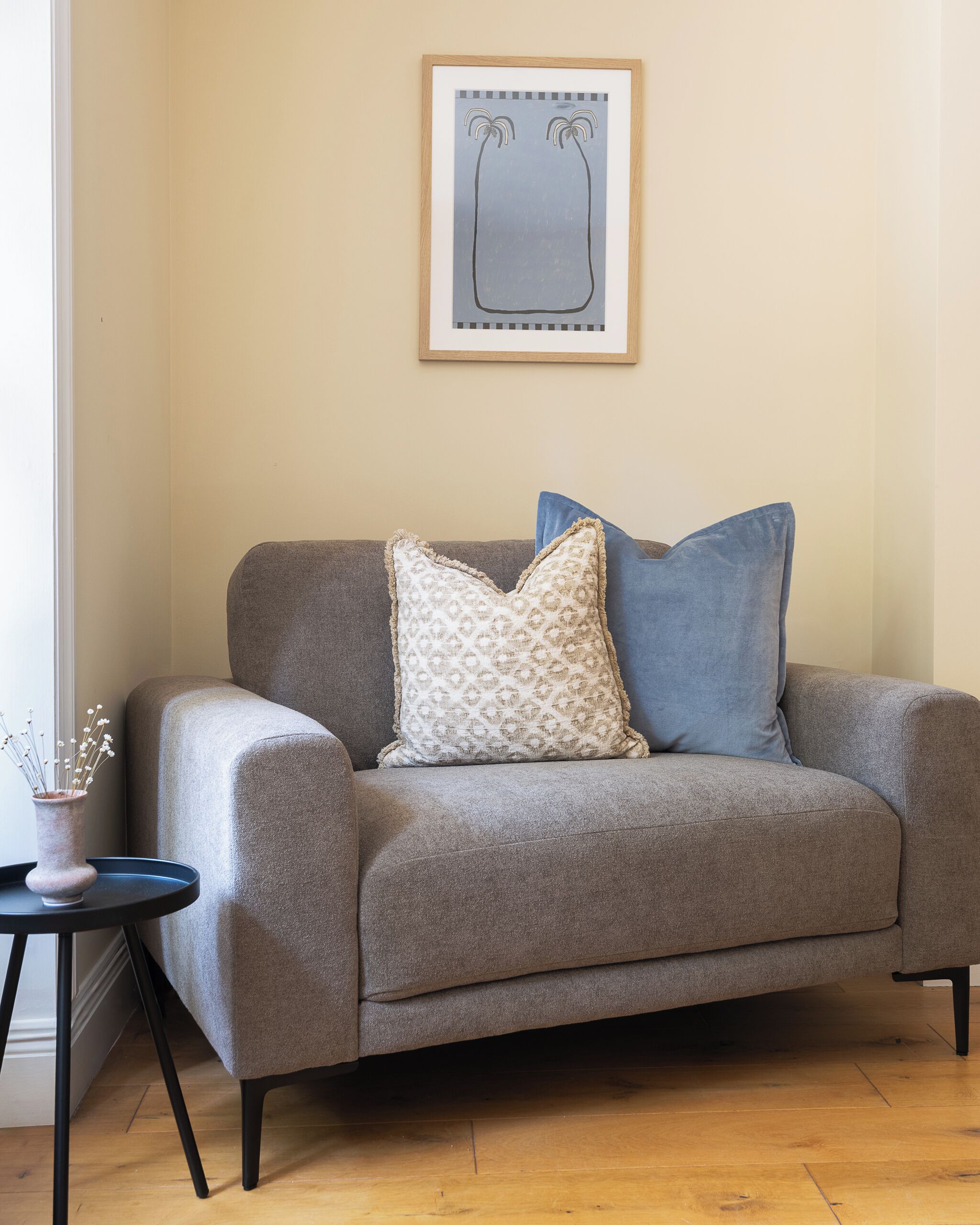 A grey sofa with patterned and solid pillows, a small side table, and a framed abstract artwork on the wall.