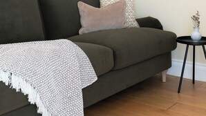 A living room with a dark green sofa, a patterned throw blanket, and a small side table with a vase. - Notting Hill Grove Apartments (London)