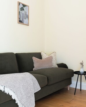 Una sala de estar con un sofá verde oscuro, un plaid estampado y una pequeña mesita auxiliar con un florero.