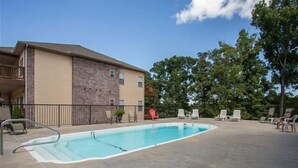 Ein Swimmingpool mit Betonumrandung, umgeben von Liegestühlen und einem Gebäude mit Backsteinfassade.
