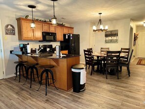 A kitchen with wooden cabinets, a central island with stools, a dining table with chairs, and pendant lighting. - 3BR lakefront condo with pool, balcony, and resort amenities (Hollister)