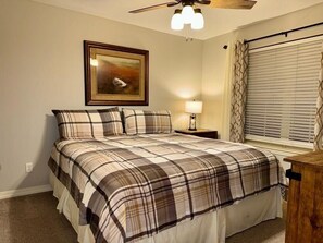 A bedroom with a bed, a nightstand, a lamp, a ceiling fan, a window with blinds, and a framed picture on the wall. - 3BR lakefront condo with pool, balcony, and resort amenities (Hollister)