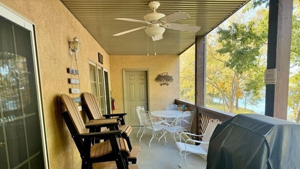 A covered patio area with outdoor seating, including a wooden chair and a table, and a grill. - Lakefront Condo  with Dock Access (Hollister)