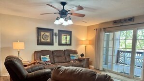 A living room with a brown leather sofa set, a ceiling fan, and a large window with a view. - Lakefront Condo  with Dock Access (Hollister)