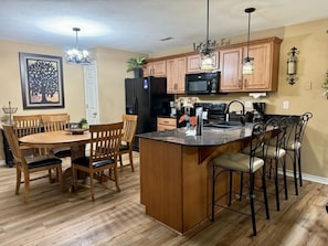 A kitchen with wooden cabinets, a central island, and a dining area with chairs. - Lakefront 3BR condo at Table Rock Lake with pool, patio, and WiFi. (Hollister)