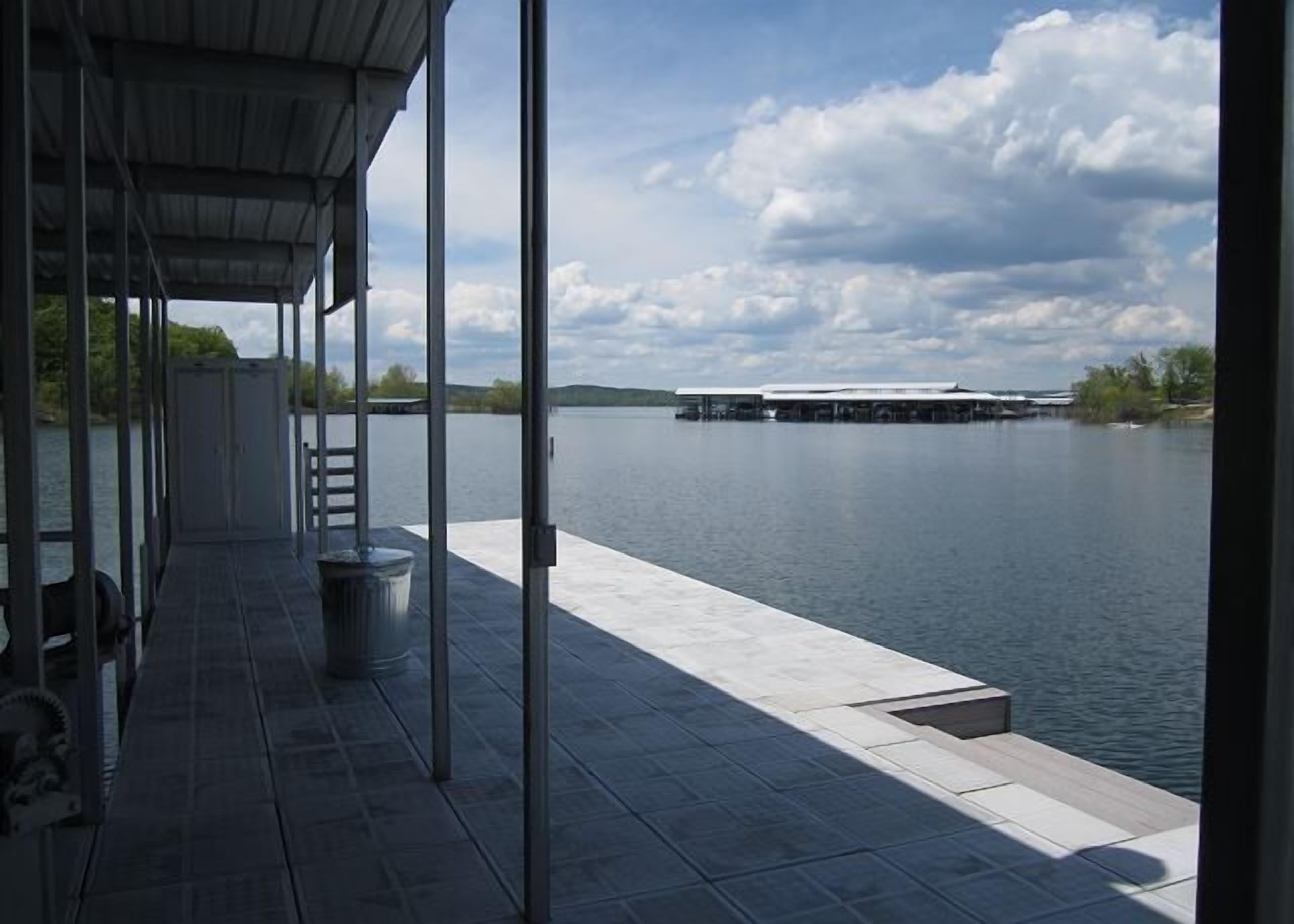 Eine überdachte Anlegestelle mit Blick auf einen stillen See und entfernte Gebäude.