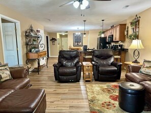 A living room with leather sofas, a coffee table, and a rug. There is a kitchen in the background with wooden cabinets and a refrigerator. - Lakefront 3BR condo at Table Rock Lake with pool, patio, and WiFi. (Hollister)