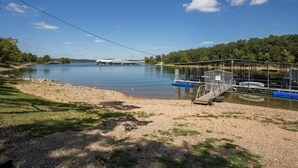 A calm lake with a dock and boats, surrounded by greenery and a clear sky. - Lakefront 3BR condo with resort pool, balcony, and Table Rock Lake views. (Hollister)