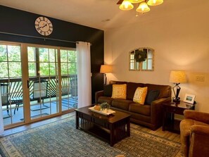 A living room with a sofa, coffee table, and lamps. There is a large window with a view of greenery. - Lakefront 3BR condo at Table Rock Lake with pool, patio, and Wi-Fi. (Hollister)