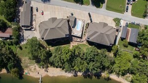 An aerial view of a residential area with two large houses, a swimming pool, and a dock extending into a body of water. - Lakefront 3BR condo at Table Rock Lake with pool, patio, and Wi-Fi. (Hollister)